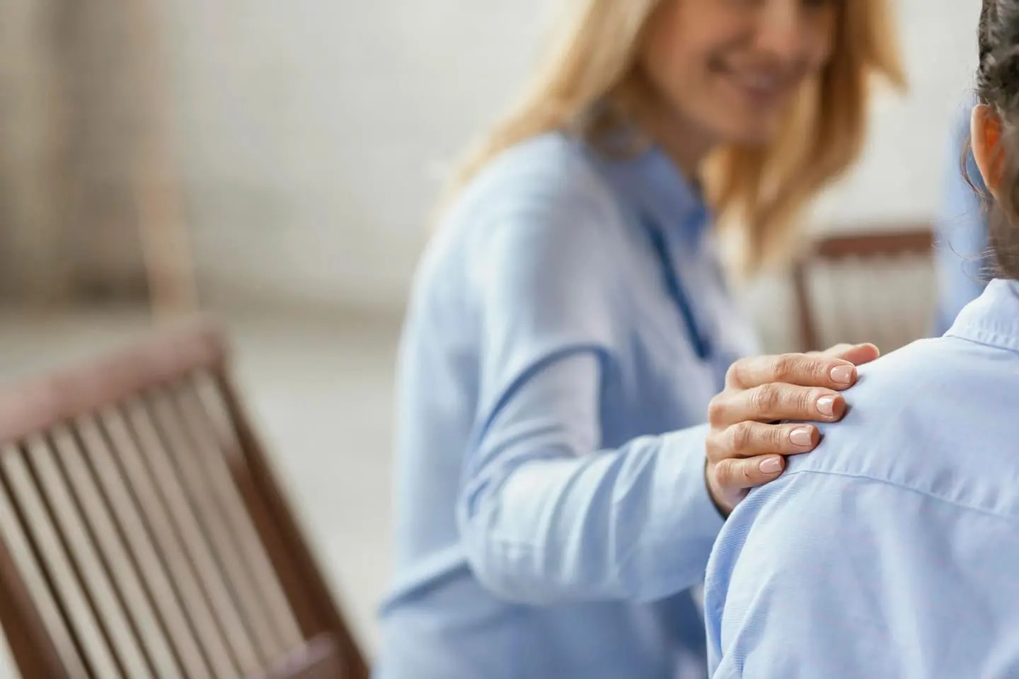 Duas pessoas frente a frente, onde uma toca gentilmente o ombro da outra que está de costas, em um gesto de apoio, conexão humana e conforto.